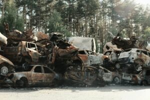 A pile of rusted, destroyed cars abandoned in a forest junkyard, symbolizing waste and decay.
